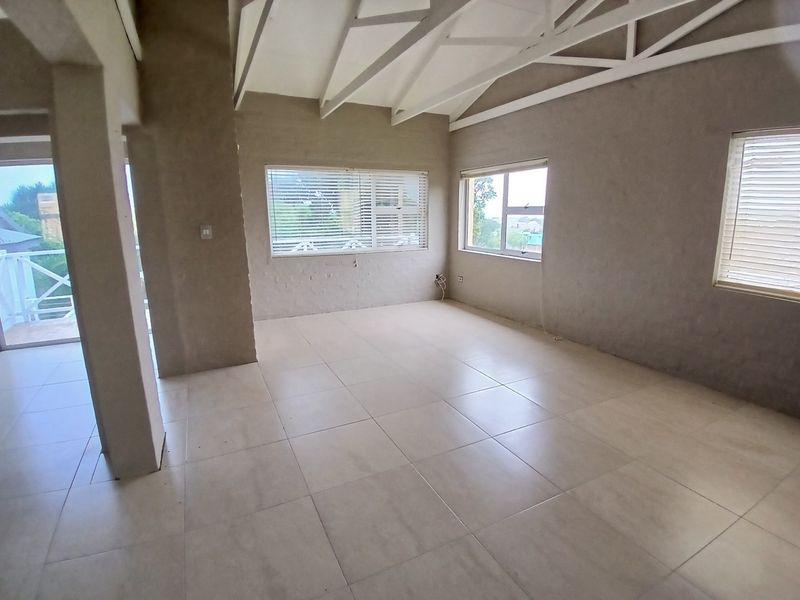 Spacious open-plan living area featuring exposed white roof trusses, large tiled flooring, and multiple windows with venetian blinds, awaiting final wall finishes.