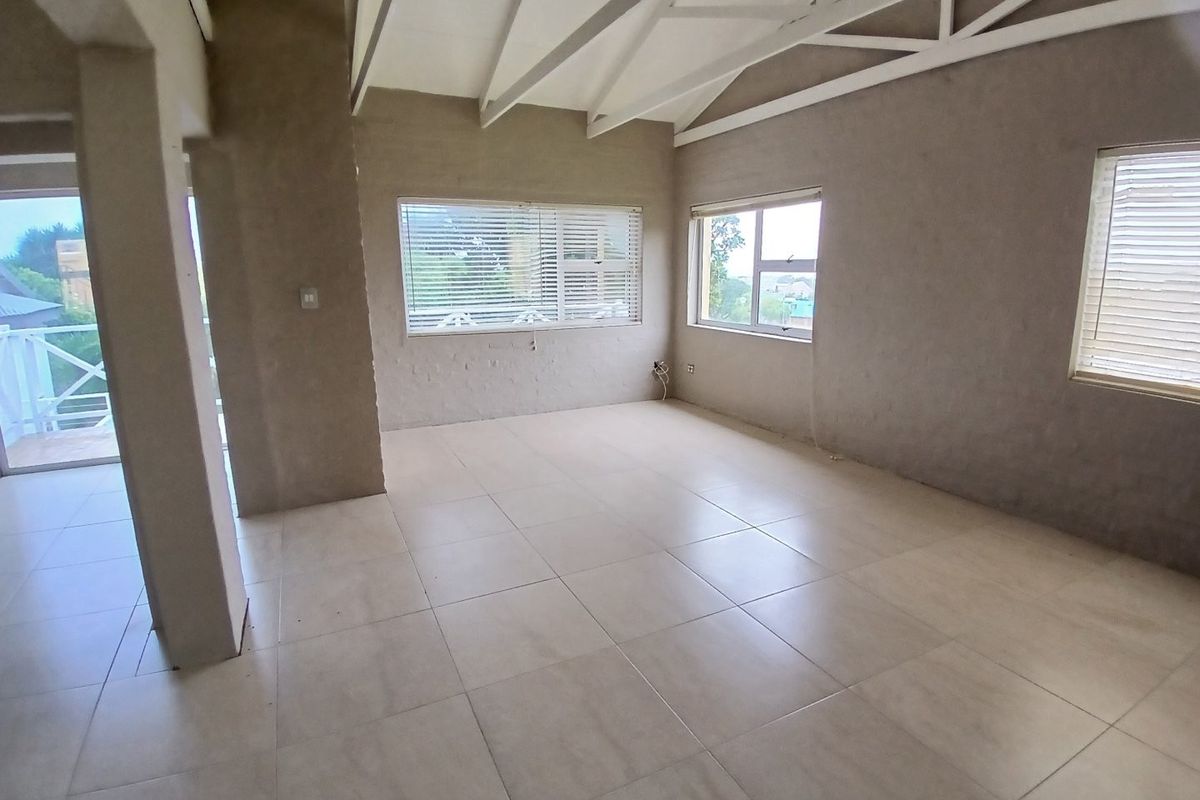 Spacious open-plan living area featuring exposed white roof trusses, large tiled flooring, and multiple windows with venetian blinds, awaiting final wall finishes.