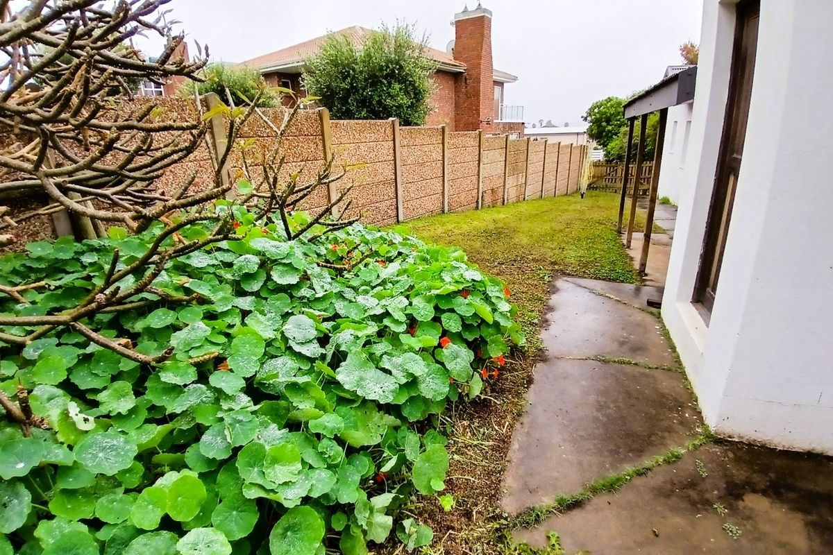 A rear garden area featuring a concrete pathway, a covered patio section, and a precast concrete boundary wall.