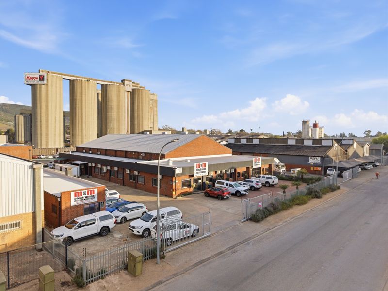 Aerial view of an industrial property featuring brick warehouse buildings, paved parking, and secure perimeter fencing in an established industrial zone.