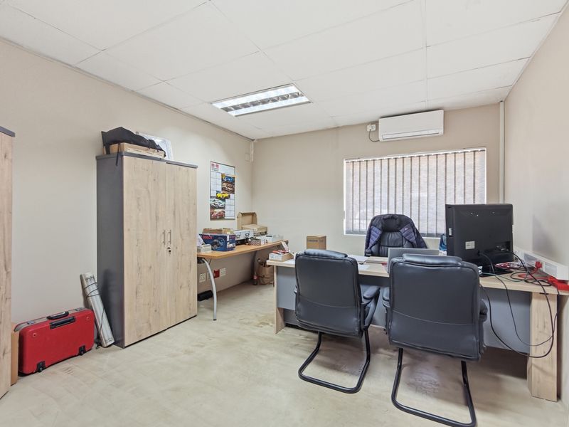 A functional industrial office space featuring a suspended ceiling, recessed lighting, wall-mounted air conditioning, and vertical blinds.