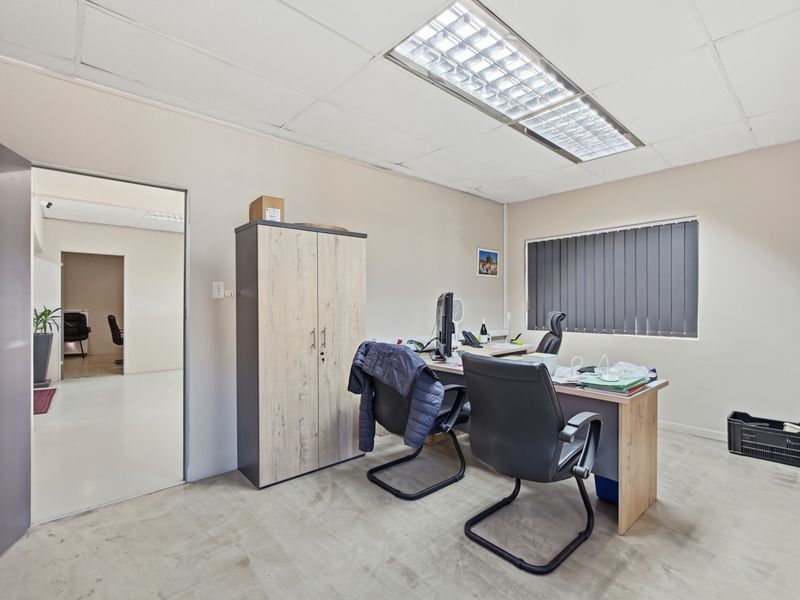 A functional office space featuring a suspended ceiling with recessed lighting, vertical blinds, and durable concrete flooring, suitable for professional use.