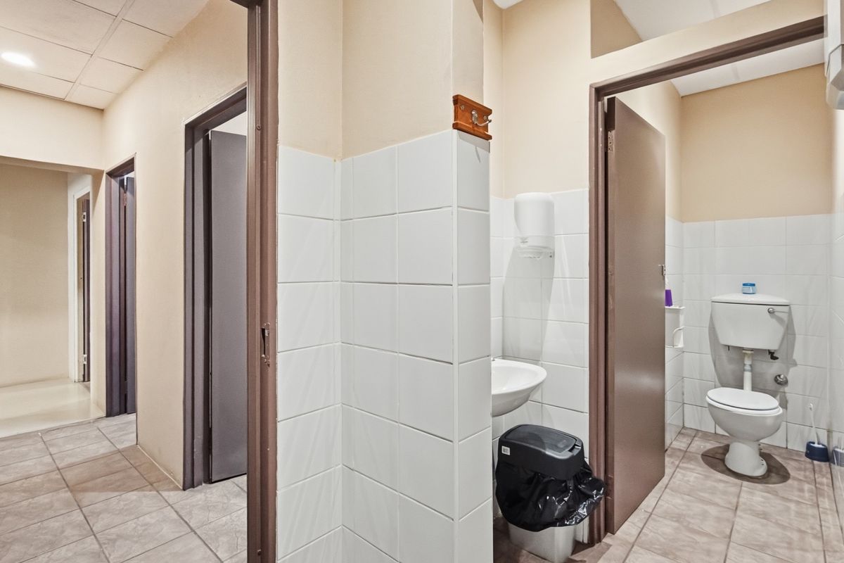 A functional industrial bathroom facility featuring tiled flooring, a wall-mounted basin, and a standard toilet with tiled splashbacks.