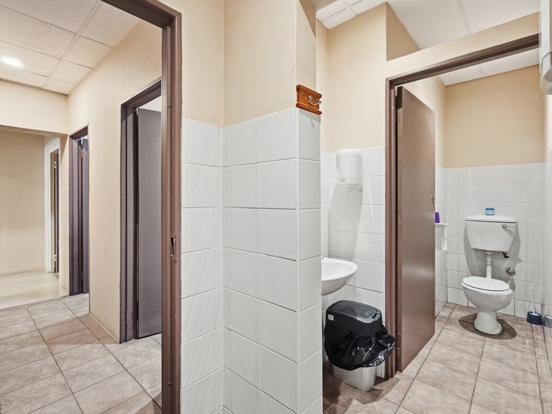 A functional industrial bathroom facility featuring tiled flooring, a wall-mounted basin, and a standard toilet with tiled splashbacks.