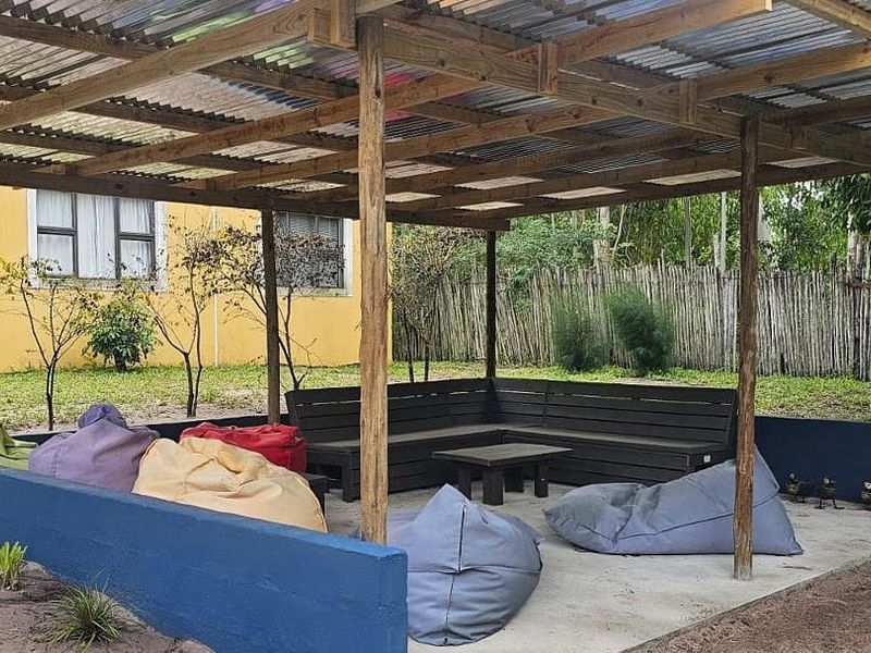 Outdoor covered patio area featuring a timber pergola structure, concrete flooring, and built-in bench seating, set within a garden environment.