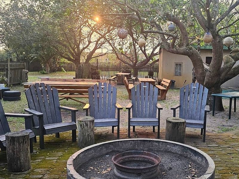 Outdoor entertainment area featuring a brick-paved patio with a central built-in fire pit, surrounded by mature trees and wooden perimeter fencing.
