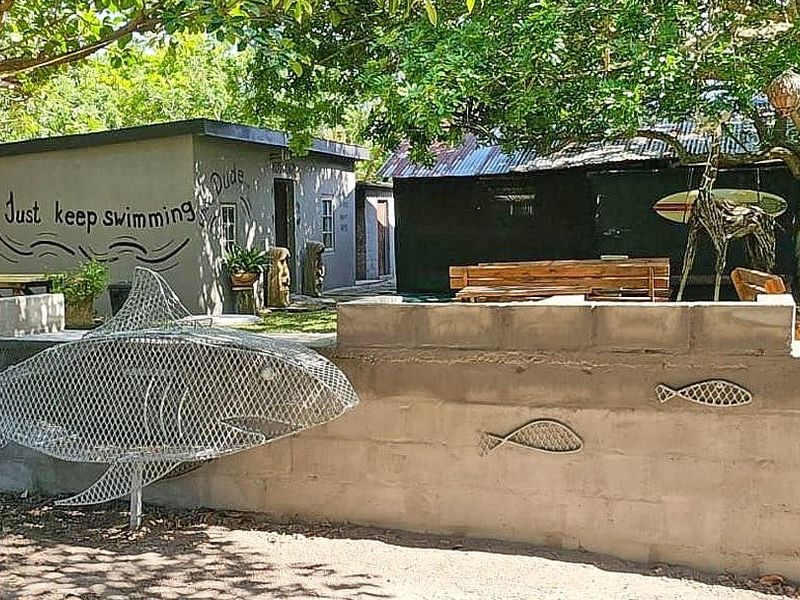 A rustic outdoor area featuring a concrete block boundary wall with decorative metal sculptures and a view toward secondary lodge outbuildings.