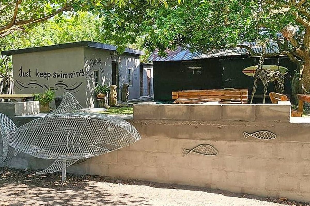 A rustic outdoor area featuring a concrete block boundary wall with decorative metal sculptures and a view toward secondary lodge outbuildings.