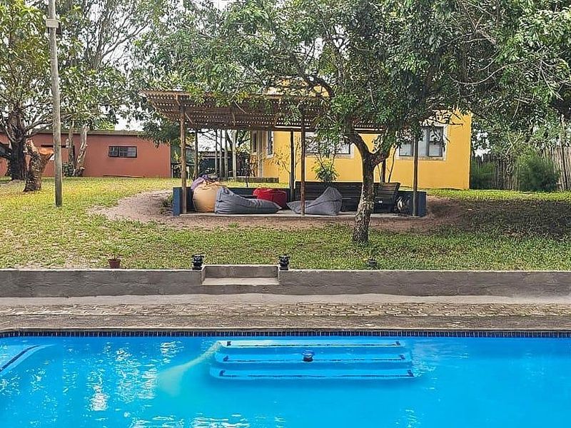 Outdoor pool area featuring a swimming pool with tiled surround, a concrete retaining wall, and a shaded pergola structure set within a garden.