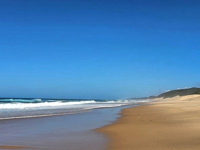 A scenic panoramic view of the pristine sandy coastline, ocean waves, and natural dunes.