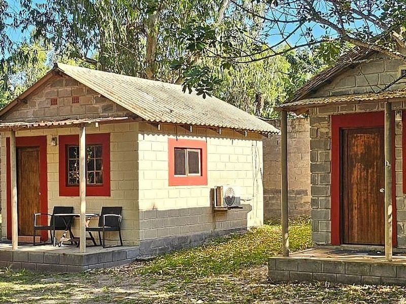 Two detached lodge units featuring concrete block construction, corrugated metal roofing, and covered patios with timber doors and window frames.