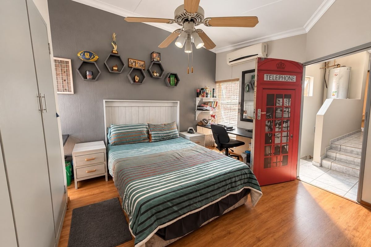 A well-maintained bedroom featuring laminate flooring, a ceiling fan, split-system air conditioning, and built-in storage cupboards.