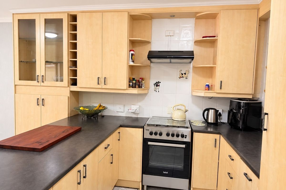 A functional kitchen featuring light-wood cabinetry, dark countertops, a tiled backsplash, and a freestanding stove with an integrated extractor fan.