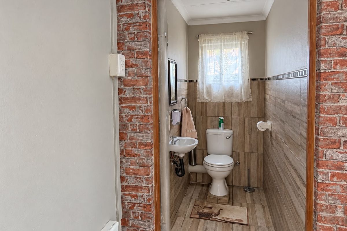 Compact bathroom featuring tiled walls, an exposed brick accent wall, a wall-mounted basin, and a standard toilet.