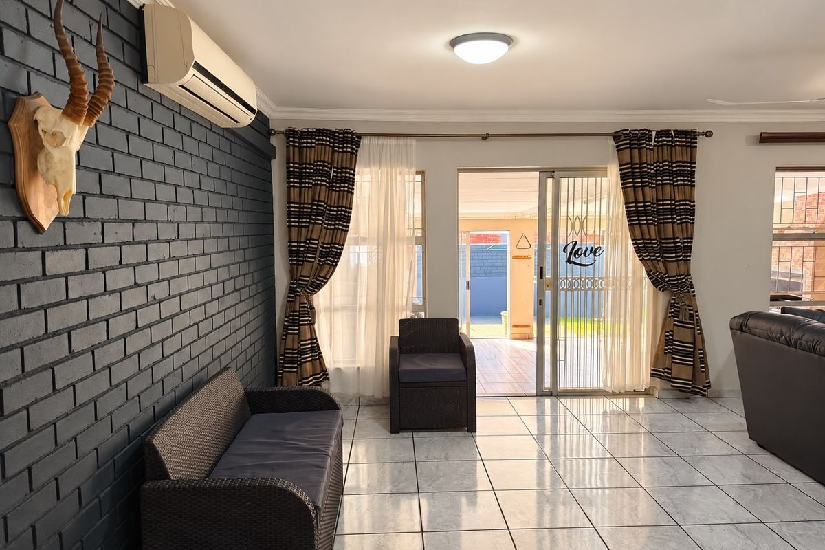 Spacious living room featuring a painted brick accent wall, split-system air conditioning, tiled flooring, and direct access to the outdoor patio area.