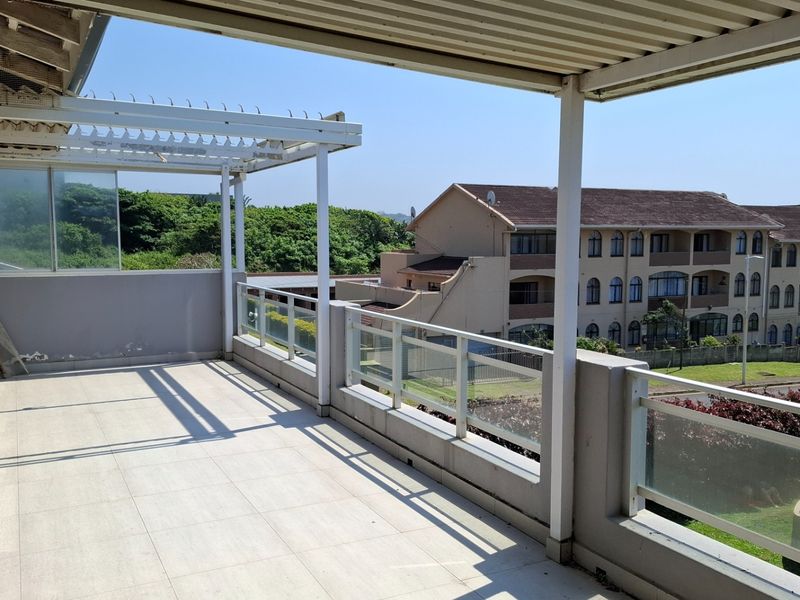 A spacious covered balcony featuring tiled flooring, a modern glass balustrade, and a pergola, offering an open outdoor area for relaxation.