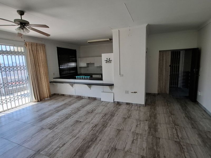 Spacious open-plan living and kitchen area featuring tiled flooring, a ceiling fan, and direct access to a balcony through a secure sliding door.