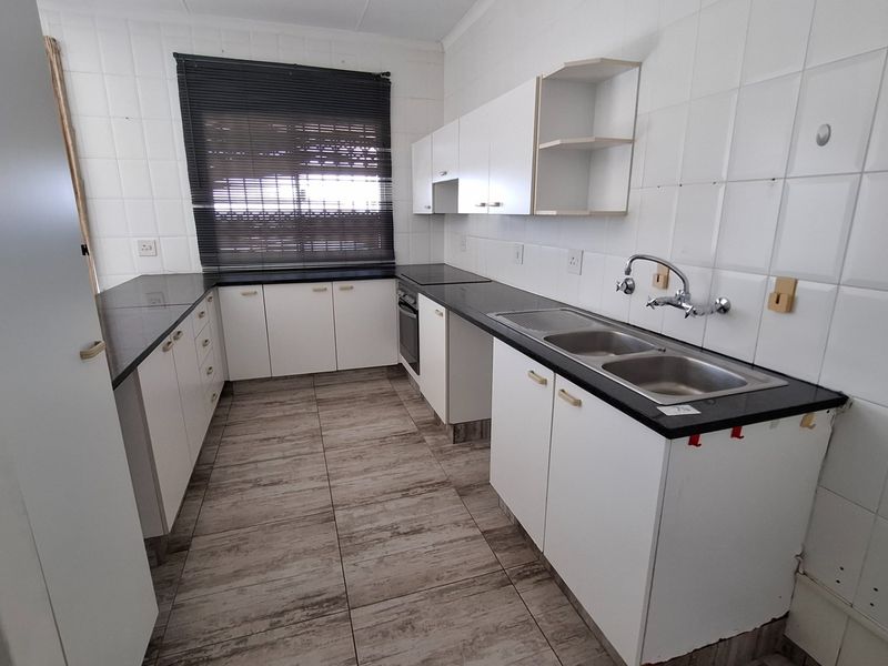 A functional kitchen featuring white cabinetry, dark countertops, a double basin sink, and tiled finishes throughout.