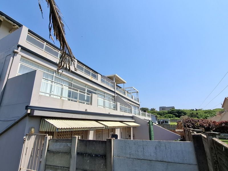 Rear elevation of a multi-story apartment building featuring multiple balconies, sliding glass doors, and protective awnings over the lower level.