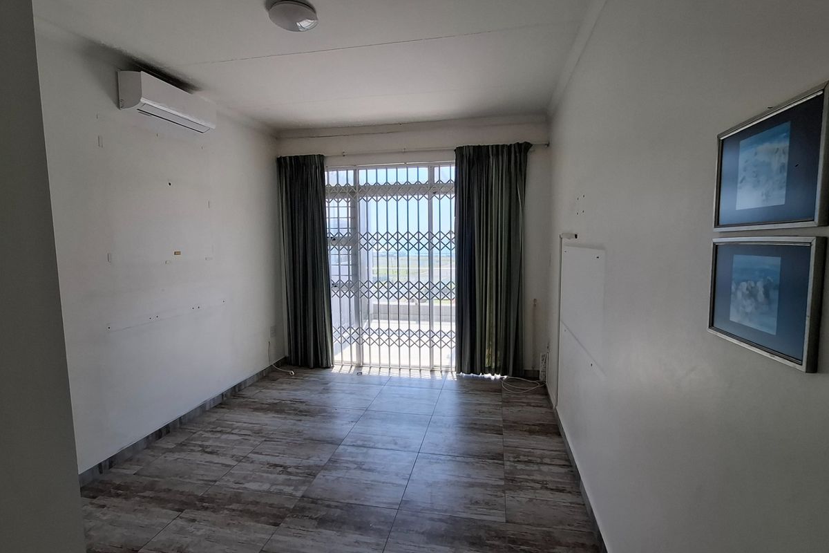 An empty living room featuring tiled flooring, a wall-mounted air conditioning unit, and a security gate leading to an outdoor area.