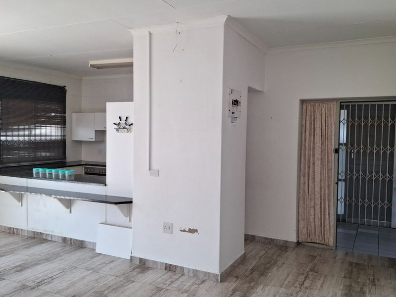 Open plan living area featuring a breakfast bar, kitchen cabinetry, and tiled flooring, with a secure entrance gate and visible wall maintenance required.