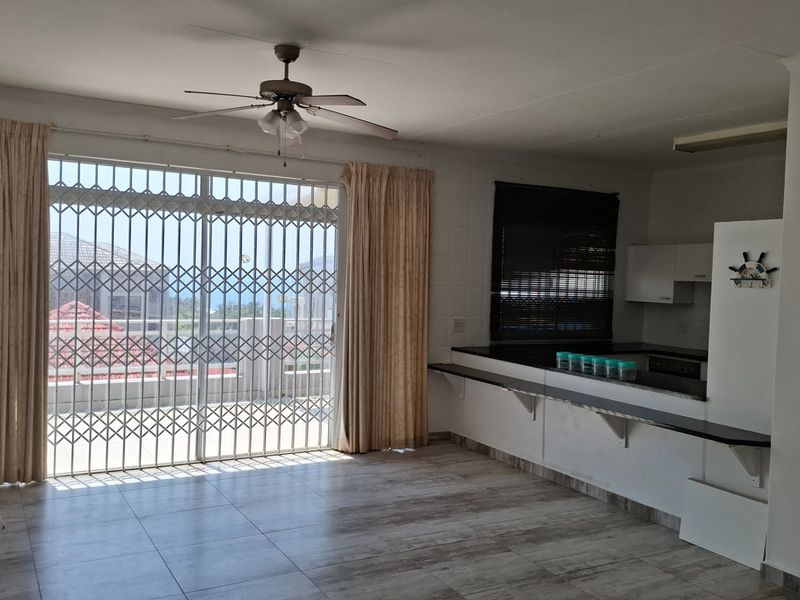 Open plan living and kitchen area featuring tiled floors, a ceiling fan, and a sliding door with security gate leading to a balcony.
