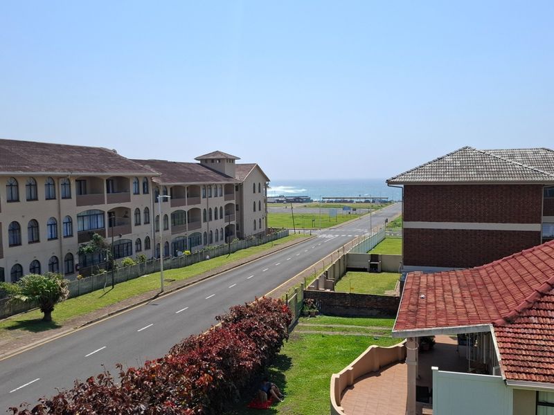 Elevated view overlooking a residential street, apartment complexes, and the distant coastline.