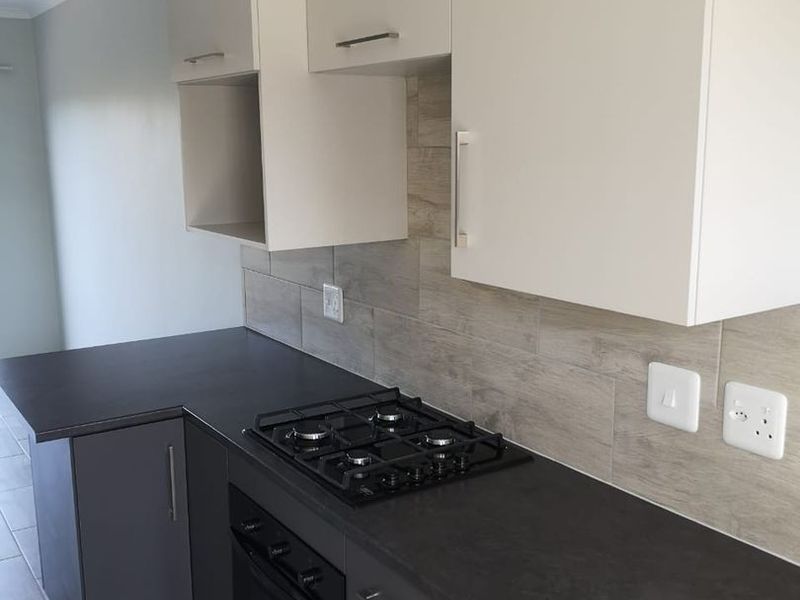 Modern kitchen featuring dark grey cabinetry, contrasting light upper cabinets, gas hob, built-in oven, and neutral tiled backsplash.