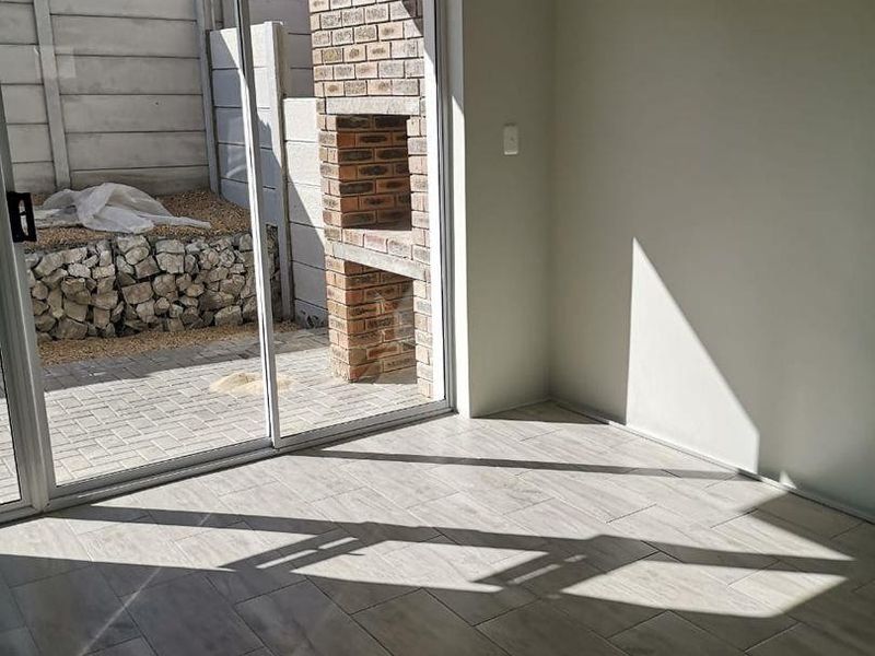 Bright living area featuring modern tiled flooring and large sliding glass doors opening onto a private paved patio with a built-in brick braai.