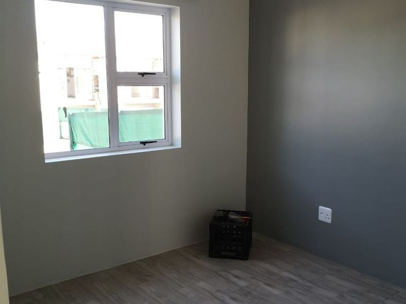 A clean, empty bedroom featuring modern wood-look floor tiles, a neutral color palette with a grey accent wall, and an aluminium window frame.