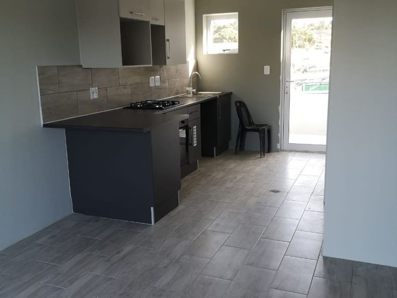 A clean, modern kitchen featuring dark cabinetry, a gas hob, built-in oven, tiled backsplash, and direct access to an outdoor area.