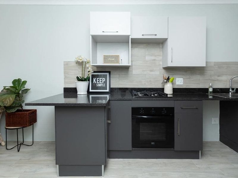 Modern kitchen featuring dark grey base cabinets, white wall units, granite countertops, a gas hob, built-in oven, and a tiled backsplash.