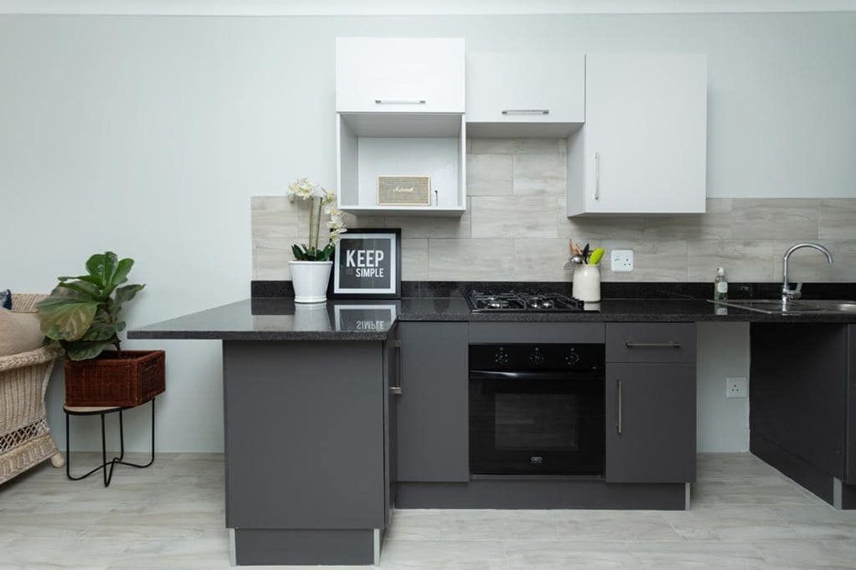 Modern kitchen featuring dark grey base cabinets, white wall units, granite countertops, a gas hob, built-in oven, and a tiled backsplash.