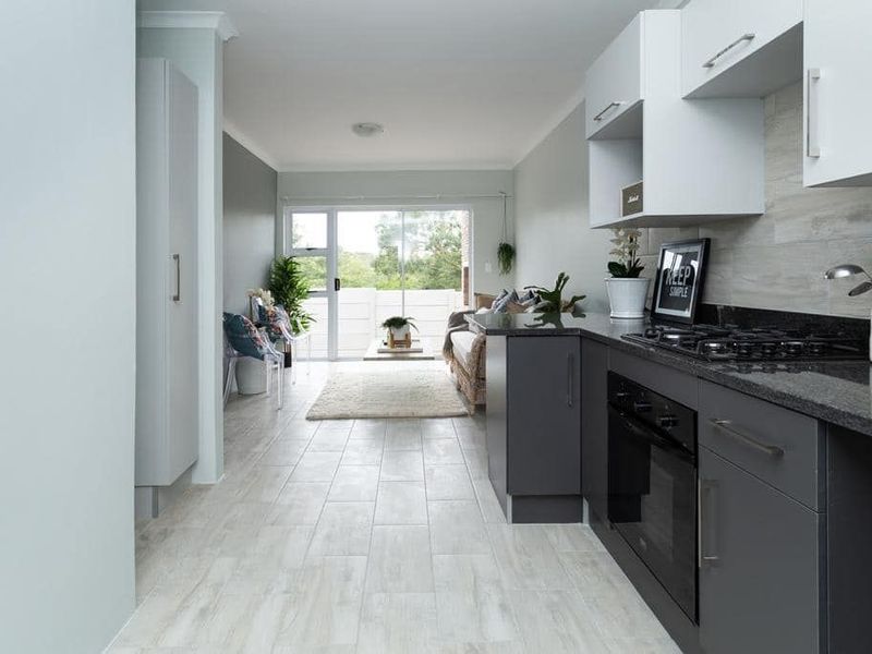 Modern open-plan kitchen and living area featuring sleek cabinetry, granite countertops, gas hob, and direct access to a balcony through sliding glass doors.