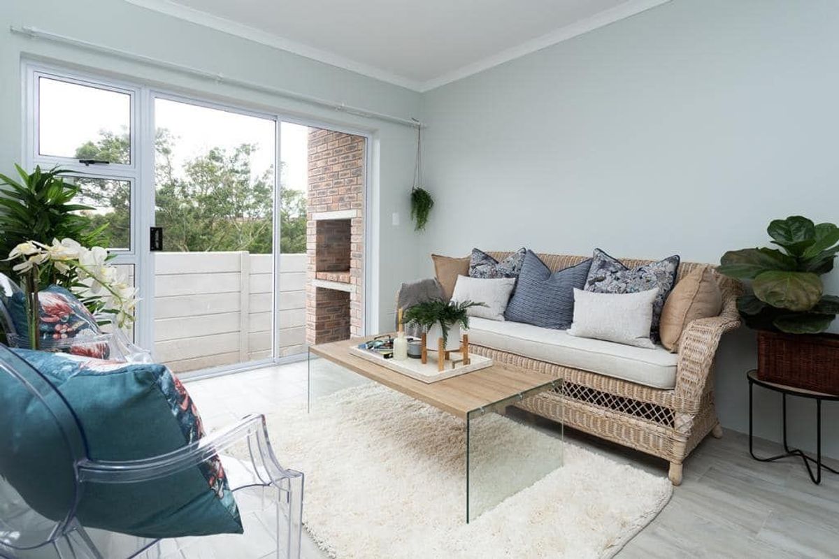 Bright living room featuring tiled flooring and a sliding glass door that opens onto a patio with a built-in brick braai.