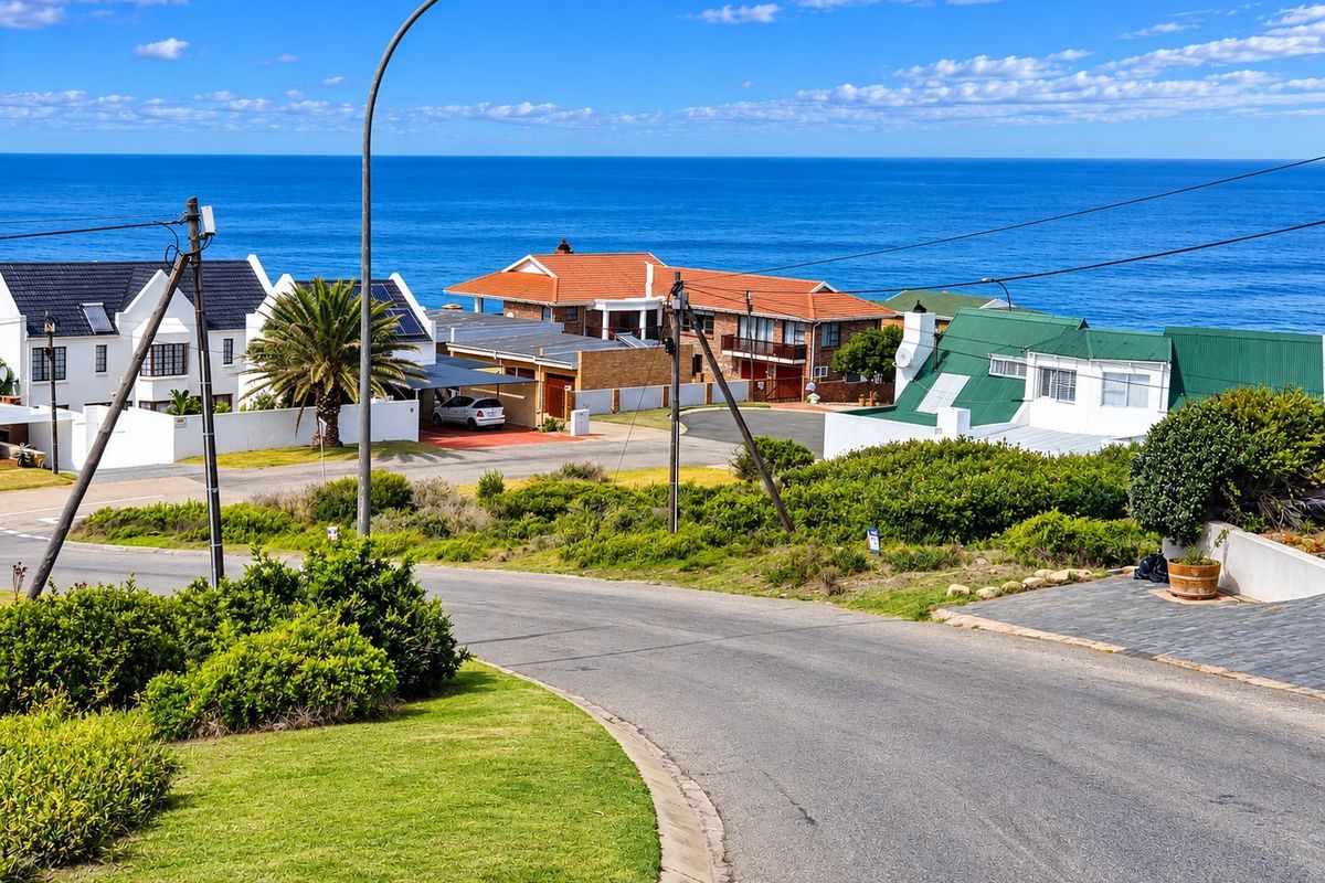 A street-level view of a residential neighborhood featuring paved roads, landscaped verges, and coastal views in the background.