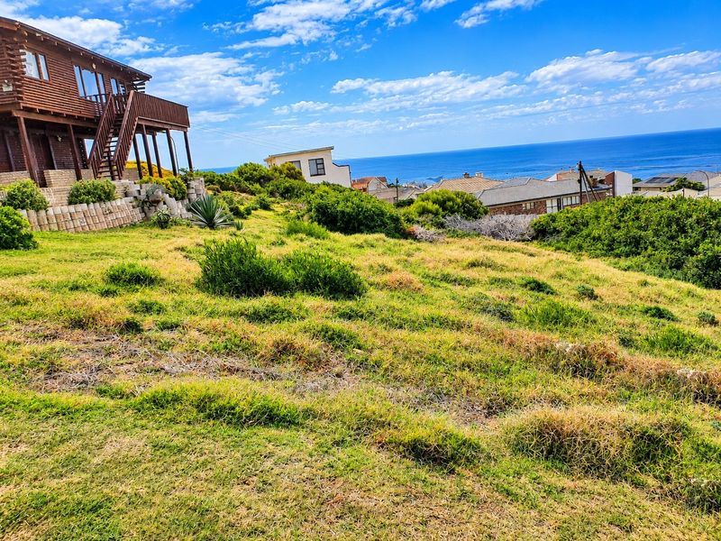 A sloped residential plot featuring established landscaping, a retaining wall, and expansive ocean views overlooking the surrounding neighborhood.