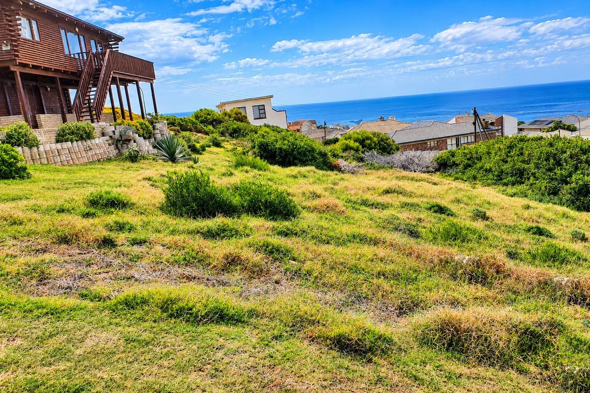A sloped residential plot featuring established landscaping, a retaining wall, and expansive ocean views overlooking the surrounding neighborhood.