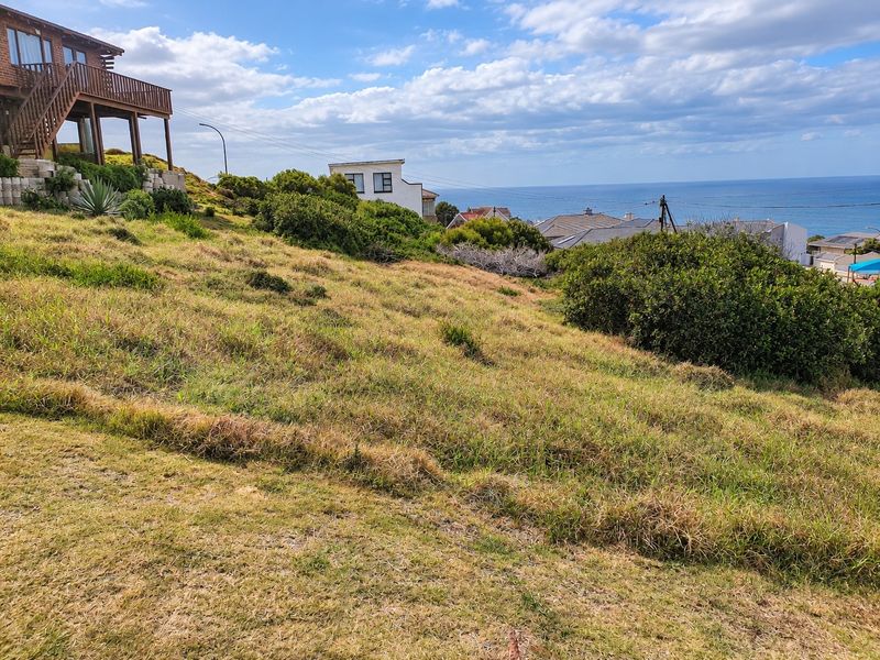 A view of the sloped residential land with coastal scenery and surrounding neighborhood properties in the background.