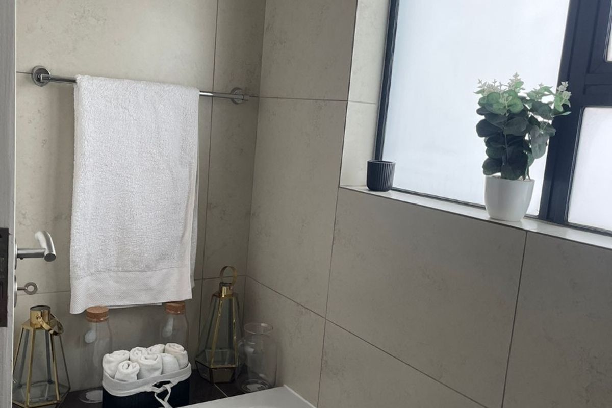 A clean bathroom featuring a built-in bathtub, neutral wall tiling, and a frosted window for privacy.