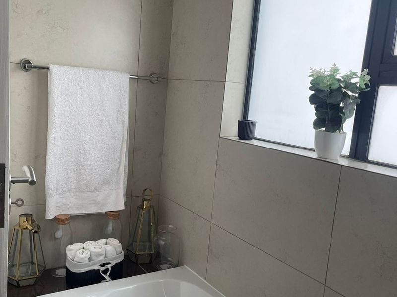 A clean bathroom featuring a built-in bathtub, neutral wall tiling, and a frosted window for privacy.