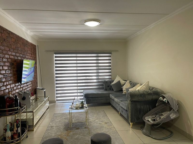 A comfortable living room featuring an exposed brick accent wall, neutral tiled flooring, and modern roller blinds, creating a warm and inviting atmosphere.