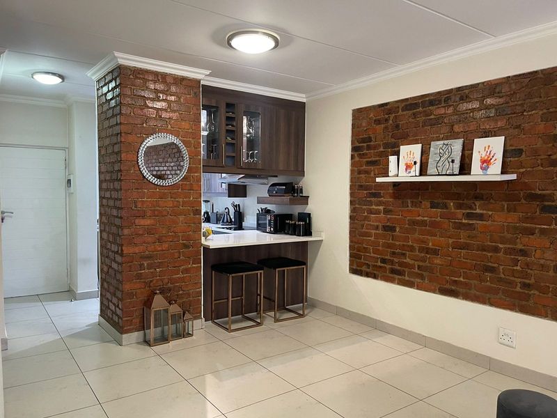 Modern kitchen area featuring a striking exposed brick feature wall, sleek built-in cabinetry, stone countertops, and clean tiled flooring.