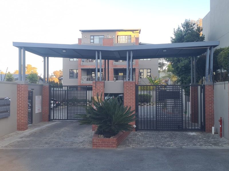 Secure gated entrance to the townhouse complex featuring a modern metal canopy, brick pillars, and paved driveway access.
