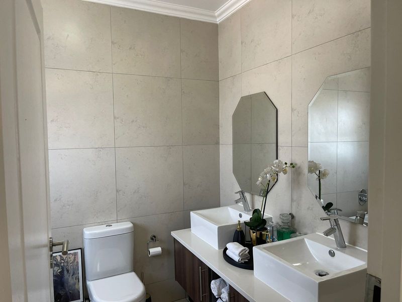 Modern bathroom featuring dual vessel sinks, a sleek vanity cabinet, large format wall tiles, and contemporary chrome fixtures.