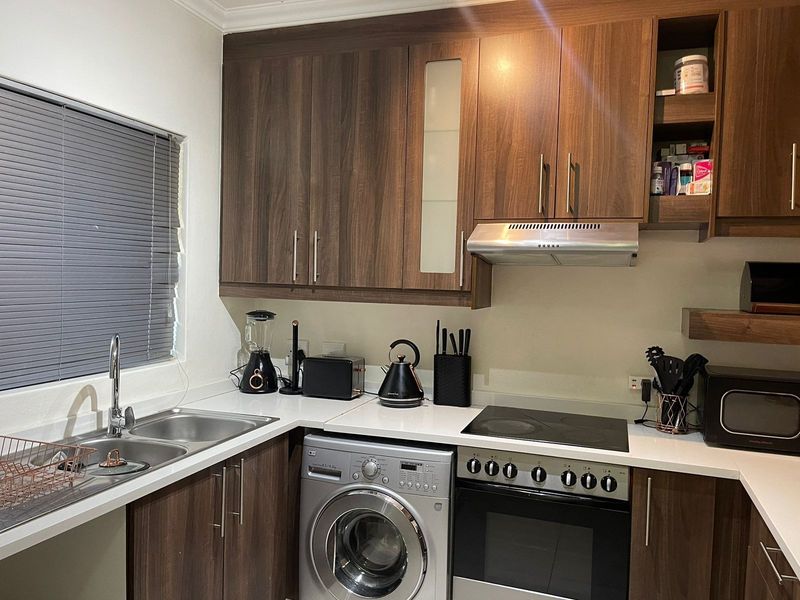 A functional kitchen featuring dark wood-look cabinetry, a stainless steel sink, integrated electric hob, oven, and extractor fan with modern finishes.