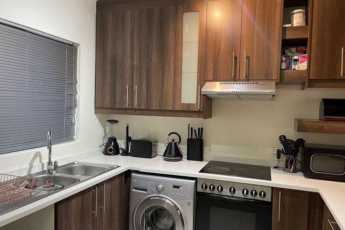 A functional kitchen featuring dark wood-look cabinetry, a stainless steel sink, integrated electric hob, oven, and extractor fan with modern finishes.