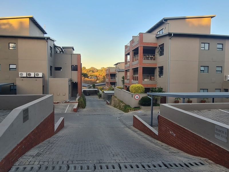 A view of the townhouse complex entrance featuring paved driveways, brick retaining walls, and multi-story residential blocks with balconies and covered parking.