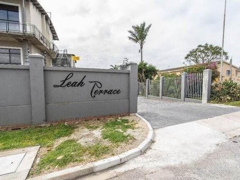 Entrance view of Leah Terrace apartment complex featuring a perimeter wall, security fencing, and paved driveway access.