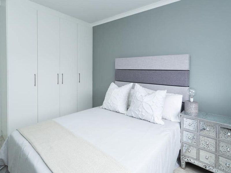 A well-maintained bedroom featuring neutral grey walls, white built-in cupboards, and decorative coving, offering a clean and modern living space.